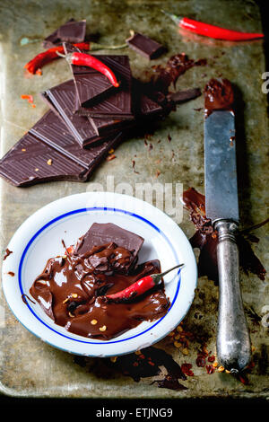 Weißen Teller mit dunklen Schokolade schmelzen und Zerkleinern von Schokolade mit frischen und trockenen red hot Chili Peppers und Vintage Messer über alte Stockfoto