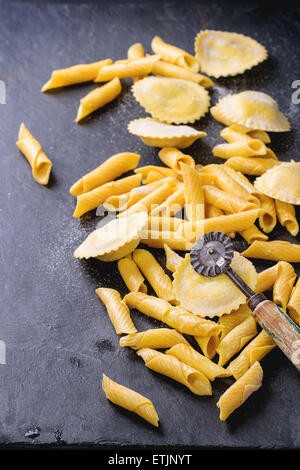 Hausgemachte Ravioli und Garganelli Nudeln mit Mehl und hölzerne Walze über schwarzem Schiefer. Selektiven Fokus Stockfoto