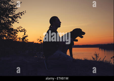 Mann mit einem Hund zu Fuß in den Sonnenuntergang am See Stockfoto
