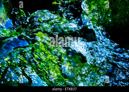 Wasser funkelt und sprudelt über grün bemoosten Felsen fließt Stockfoto