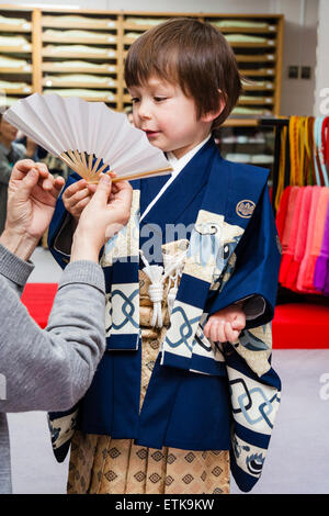 Junges asiatisch-kaukasisches Kind, Junge, 4-5 Jahre alt und in blau-goldenem Kimono gekleidet, wird für seine 3-5-7-Zeremonie in Japan ein Fan übergeben. Stockfoto