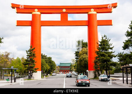 Der riesige orangefarbene Torii, der die Hauptstraße vor dem von Bäumen gesäumten Baum überspannt, nähert sich dem Heian-Schrein in Kyoto. Die Torii ragt 24 Meter hoch auf. Stockfoto