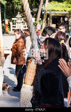 Japan, Kyoto, Yasaka Shinto Shrine, japanische junge Frau lächelt und hält das Seil in beiden Händen, um beim Beten die Glocke zu läuten. Stockfoto