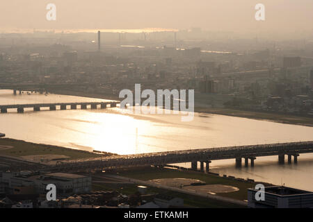 Luftbild vom Umeda Sky Building, Osaka, von Eisenbahn- und Straßenbrücken, die Kyu-Yodo, Yodo, Fluss, bei Sonnenuntergang, goldene Stunde überspannen. Hazy aufgrund von Umweltverschmutzung. Stockfoto