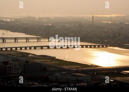 Luftbild vom Umeda Sky Building, Osaka, von Eisenbahn- und Straßenbrücken, die Kyu-Yodo, Yodo, Fluss, bei Sonnenuntergang, goldene Stunde überspannen. Hazy aufgrund von Umweltverschmutzung. Stockfoto