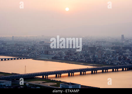 Luftbild vom Umeda Sky Building, Osaka, von Eisenbahn- und Straßenbrücken, die Kyu-Yodo, Yodo, Fluss, bei Sonnenuntergang, goldene Stunde überspannen. Hazy aufgrund von Umweltverschmutzung. Stockfoto