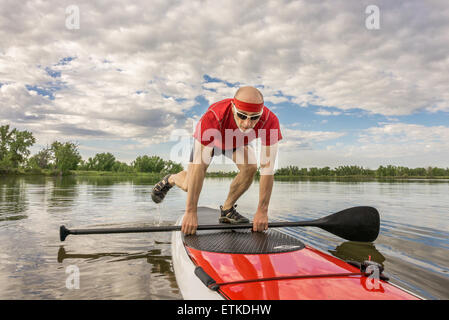 Senior männlichen Paddler ein Stand up Paddleboard - einem lokalen See in Colorado unter bewölktem Himmel sein Training ab Stockfoto