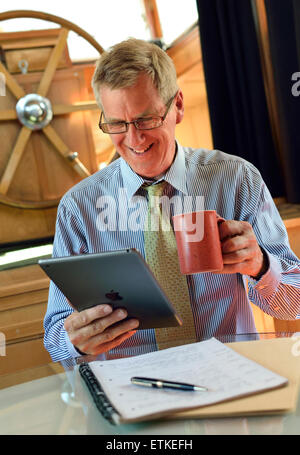 IPad Business man Online-Zoom-Teams Treffen reifen Unternehmer mit Tee Interaktion mit seinem iPad Air smart Tablet-Computer im Binnenschiff Hausboot Büro Stockfoto