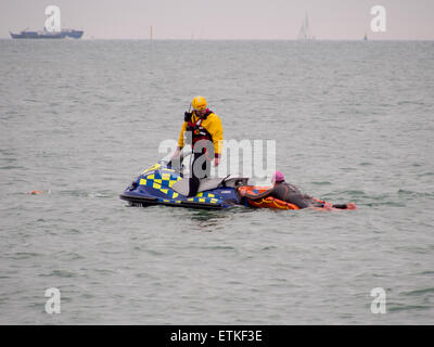 Ein Rettungsschwimmer auf einem Jetski hilft einen Schwimmer, die in Schwierigkeiten stecken, während einer Triathlon-Veranstaltung im Solent Stockfoto