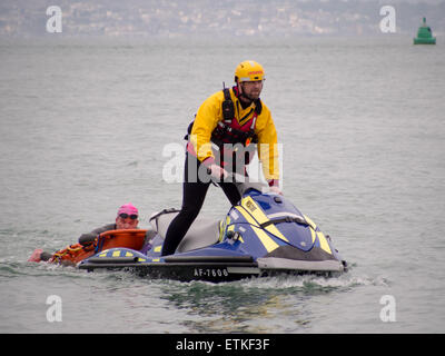 Ein Rettungsschwimmer auf einem Jetski hilft einen Schwimmer, die in Schwierigkeiten stecken, während einer Triathlon-Veranstaltung im Solent Stockfoto