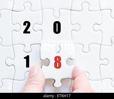 Hand eines Geschäftsmannes, die Vollendung des Puzzles mit das letzte fehlende Stück. Konzept-Bild Puzzle Board mit Jahr 2018 Stockfoto