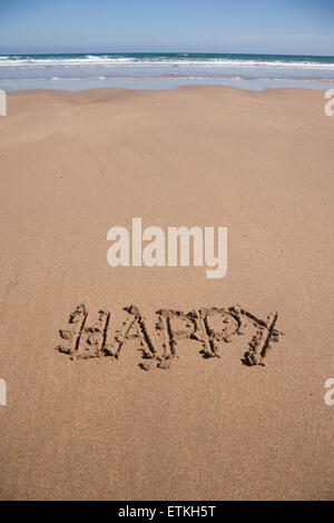 glückliches Wort geschrieben am braunen Sandboden Ebbe Strand Meeresküste in Spanien Europa Stockfoto