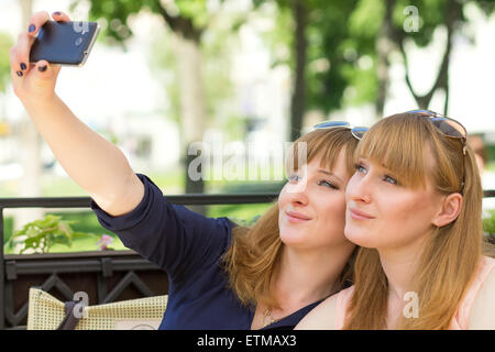 Zwei Zwillinge Mädchen, die Selfie in Restaurant am sonnigen Sommertag. Junge hübsche Schwestern auf der Terrasse des café Stockfoto