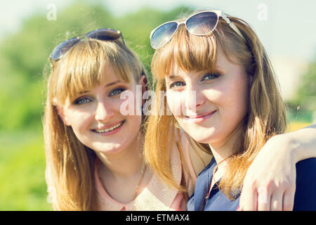 Hübsche Zwillinge Mädchen, die Spaß an outdoor-Sommer-Park. Junge lächelnde Frauen mit Brille in der Kamera suchen. Warme Farbe getönt Bild Stockfoto