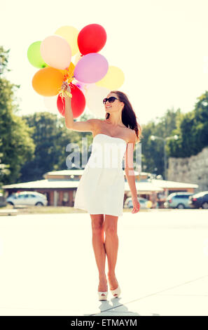 lächelnde junge Frau mit Sonnenbrille mit Luftballons Stockfoto