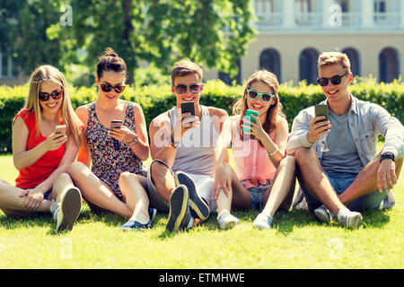 lächelnden Freunde mit Smartphones auf dem Rasen sitzen Stockfoto