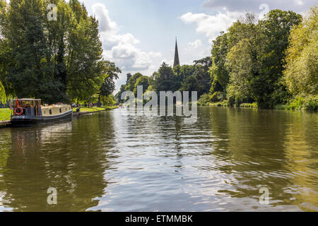 Fluß Severn durchquert Stratford-upon-Avon mit langen Boot vertäut am linken Ufer mit Bäumen und einer Kirche in der Ferne. Stockfoto