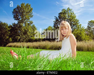 kleines Mädchen sitzt auf dem grünen Rasen Stockfoto