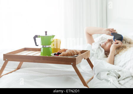 Frühstück Holztablett mit Kaffee und Gipfeli auf Bett. Romantische Überraschung für aufwachen Frau mit schlafen Augenmaske Stockfoto