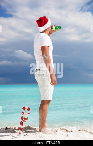 Mann im Santa Helfer Hat Blick auf das Meer und Champagner aus der Flasche trinken. Silvester Feier Stockfoto