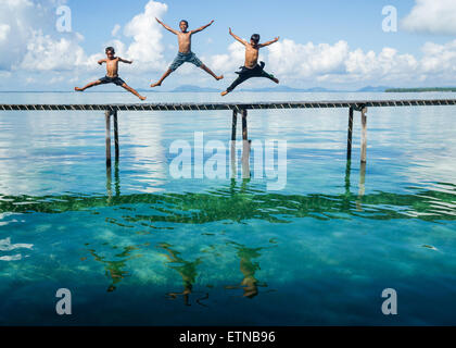 Drei Jungs springen zum Meer von einer Anlegestelle Salakan Insel, Semporna, Sabah, Malaysia Stockfoto