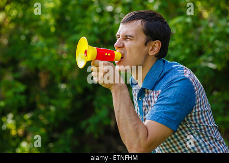 Der Mann auf der Straße hält einen Kunststoff Lautsprecher schreit auf grün Stockfoto