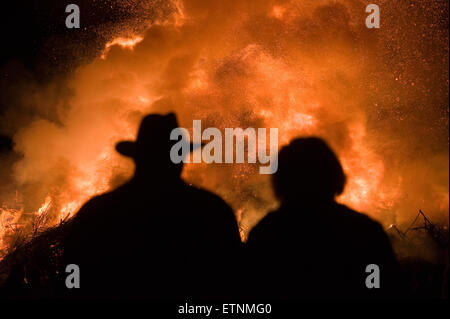 Mann mit Hut und eine Frau beobachten ein riesiges Feuer, eine Tradition mit Ostern in Nordwest-Europa. Stockfoto