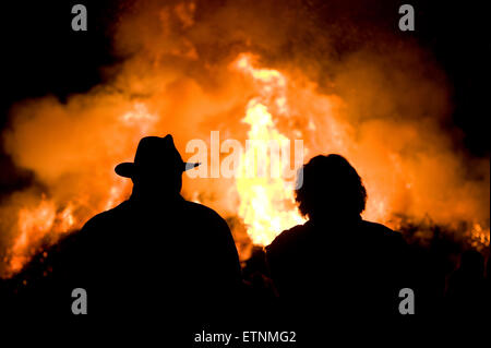 Mann mit Hut und eine Frau beobachten ein riesiges Feuer, eine Tradition mit Ostern in Nordwest-Europa. Stockfoto