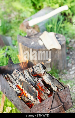 Brennholz brennt in Outdoor-Feuerschale mit Axt im Baumstumpf auf Hintergrund Stockfoto