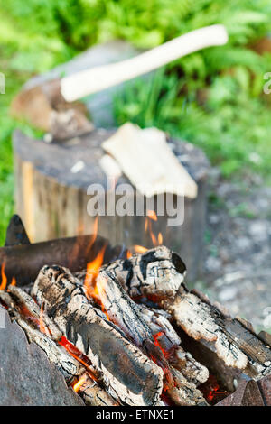 Brennholz in rostigen Kohlenbecken brennen hautnah mit Axt im Baumstumpf auf Hintergrund Stockfoto