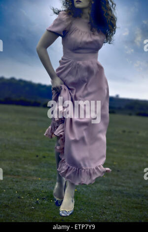 eine Frau in einem rosa Kleid läuft auf einer Wiese Stockfoto