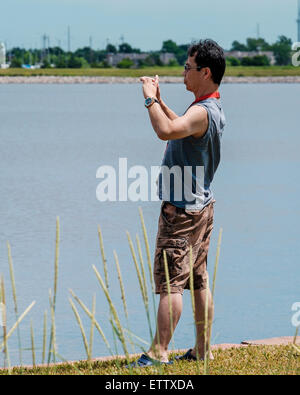 Ein 50 Jahre alter asiatischer Mann nimmt Bilder mit seinem Handy am Lake Hefner in Oklahoma City, Oklahoma, USA. Stockfoto