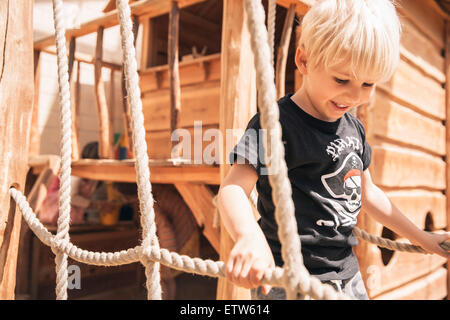 Lächelnde Knabe Hängebrücke Holzschiff am Spielplatz entlang Stockfoto