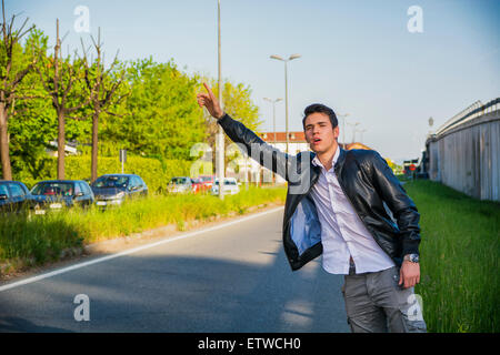 Hübscher junger Mann, ein Tramper warten Auto am Straßenrand in der Stadt, tragen schwarze Lederjacke Stockfoto