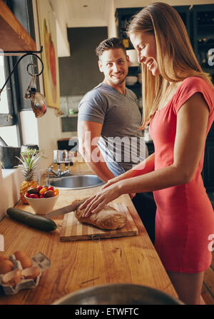 Kaukasische paar zusammen in der Küche im Morgen. Junge Frau Schneiden von Brot, während ihr Mann steht im Mittelpunkt. Sonnen Stockfoto