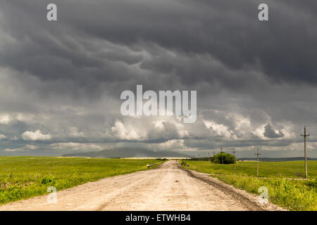 Einsamen Feldweg führt bis zum Horizont, wie dunkle Regenwolken über Kopf sammeln Stockfoto