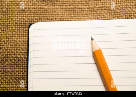 Geöffnete Notebook mit einem leeren Blatt und Bleistift auf das alte Gewebe Stockfoto