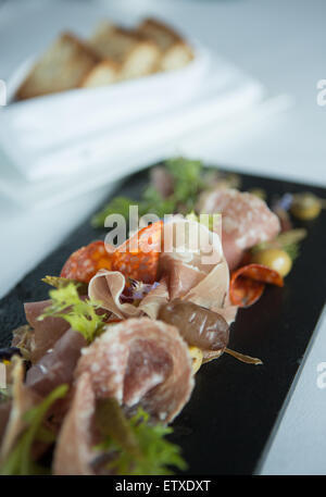 Wurst-Auswahl auch Salami, Chorzio und Parma Schinken. Serviert auf einer schwarzen Tafel mit Brot und Garnitur. Stockfoto