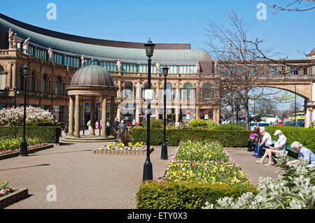 Leute, die sich im Frühling in Victoria Gardens entspannen und Victoria Shopping Centre Shops Harrogate City Centre Läden North Yorkshire England Großbritannien Stockfoto