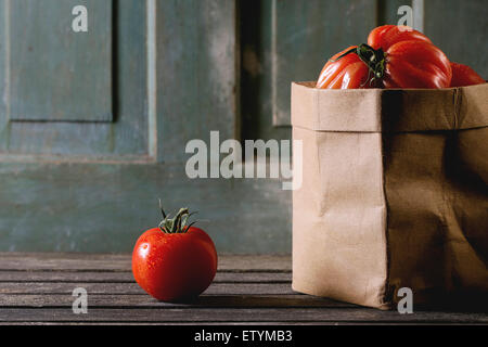 Eins und Haufen von großen roten Tomaten RAF in Papiertüte über alten Holztisch. Dunkle, rustikale Atmosphäre Stockfoto