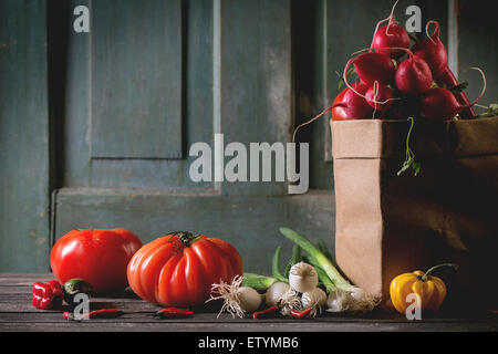 Haufen von reif bunte Frischgemüse Tomaten, Chilischoten, Frühlingszwiebeln und Bündel Radieschen in Papiertüte über alte hölzerne tab Stockfoto