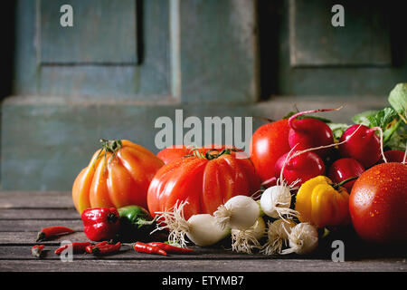 Haufen frische reife buntem Gemüse Tomaten, Chilischoten, Frühlingszwiebeln und Haufen von Rettich über alten Holztisch. Dunklen Rost Stockfoto