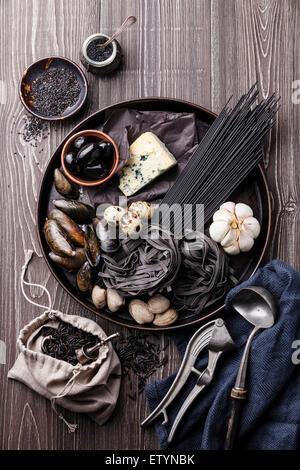 Schwarze Rohkost Zutaten - Teigwaren, Oliven, Muscheln auf hölzernen Hintergrund Stockfoto