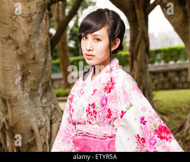 Asiatische Frau im Kimono von Bäumen im Garten Stockfoto