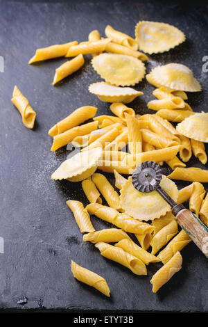 Hausgemachte Ravioli und Garganelli Nudeln mit Mehl und hölzerne Walze über schwarzem Schiefer. Stockfoto