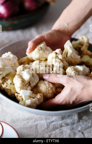 Eine Frauenhand sind Incorprating einem würzigen Dressing auf frisch geschnittenem Blumenkohlröschen. Stockfoto