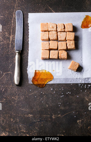 Fudge, Süßigkeiten und Karamell auf Backpapier, serviert mit Vintage Messer auf dunklem Hintergrund. Ansicht von oben Stockfoto