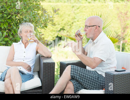 ein paar sitzt mit einem Glas in der Hand auf dem Sofa in ihrem Garten Stockfoto