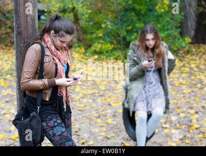 zwei Mädchen im Teenageralter auf einem Spielplatz Blick auf ihren Handys Stockfoto