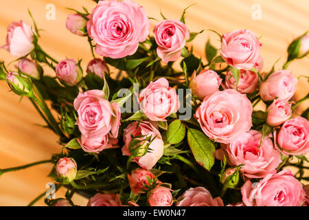 Haufen von kleinen rosa Rosen in einer Glasvase auf einem Holztisch. Stockfoto